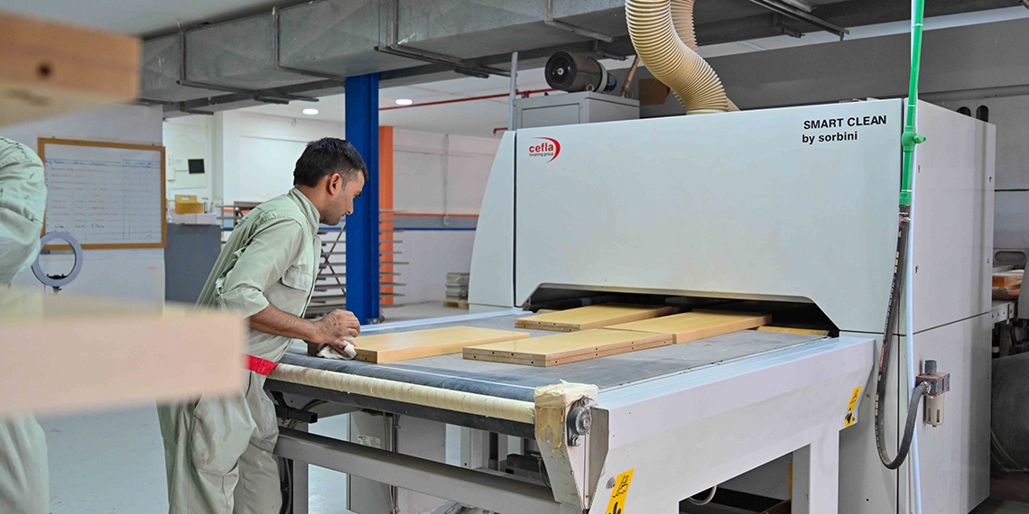 A craftsman feeding timber panels through an edge-banding machine in the Side Creations workshop